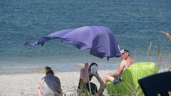 Strandbesucher am Meer unter dem Sonnenschirm.