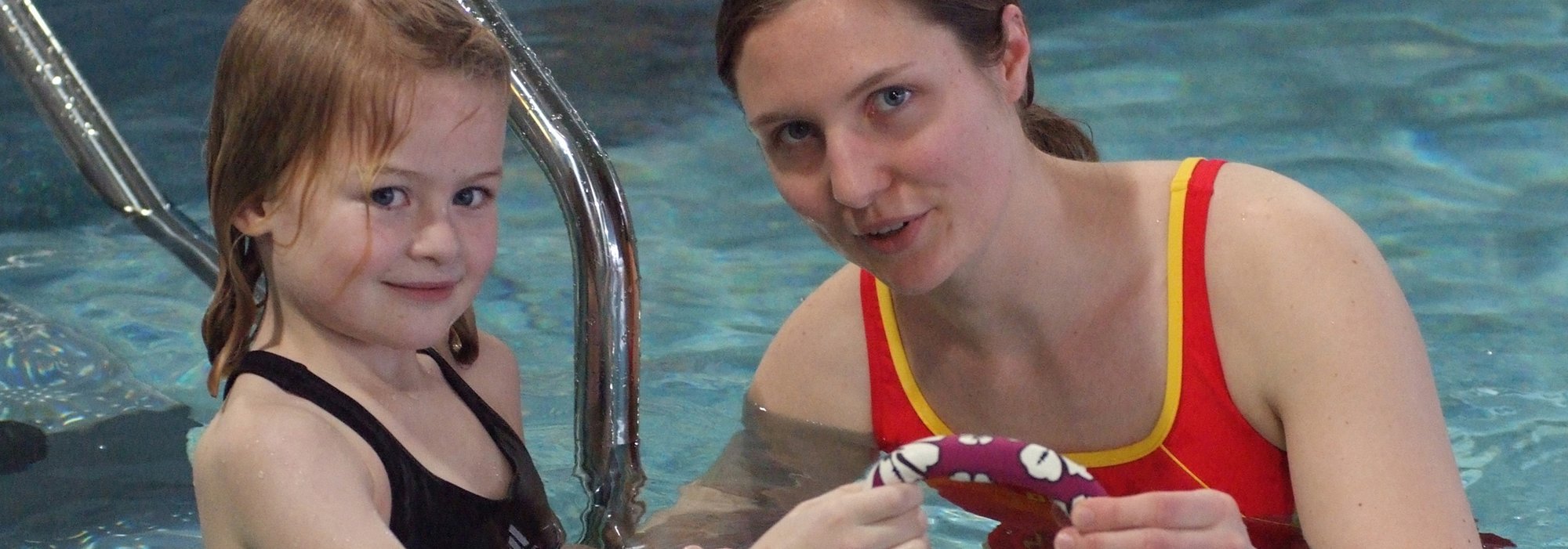 DLRG-Schwimmerin bringt einem kleinen Mädchen im Becken das Schwimmen bei.