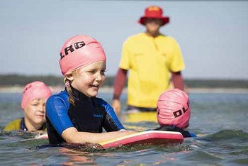 Kind mit Schwimmbrett im Meer im Vordergrund, im Hintergrund Kinder und Ausbilder