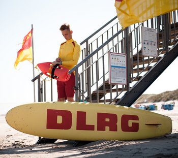 Ein Rettungsschwimmer der DLRG steht vor einer Wachstation an der Küste