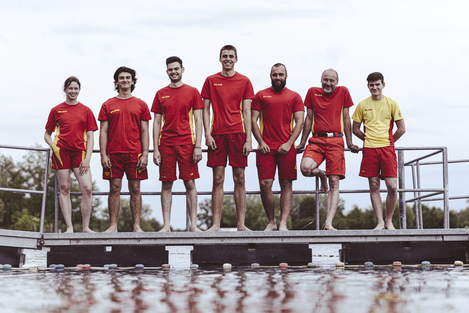 DLRG Mitglieder stehen auf einem Steg am Wasser und schauen fröhlich in die Kamera